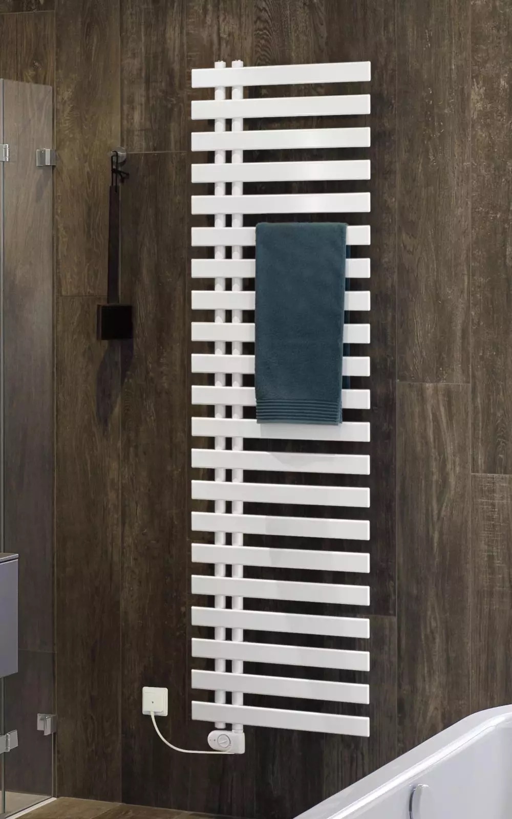 Badheizköper Cha-cha von Bemm montiert an einer dunkelbraunen Holzoptik-Wand, mit einem petrolfarbenen Handtuch darüber.