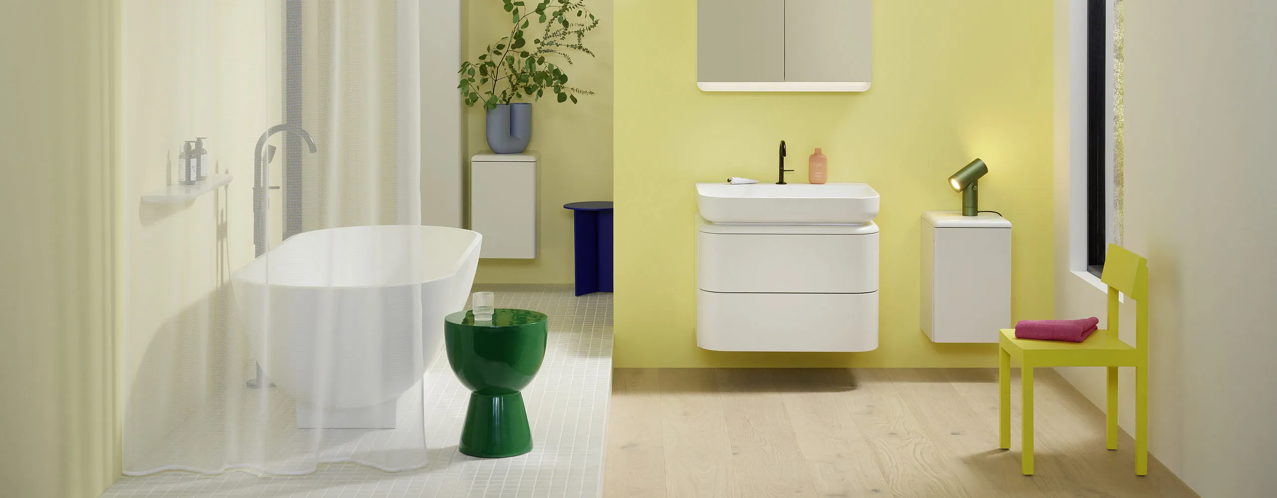 Badezimmer mit weiß-gelben Wandfarben, Holzboden, freistehender Badewanne und wandhängenden, weißen Badmöbeln der Serie b:me von burgbad.