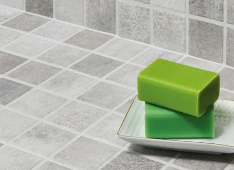 Seifenschale zwei grünen Seifen-Stücken auf einem Waschtisch mit hellgrauen Mosaikfliesen.