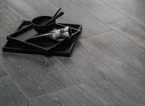  Ein eleganter grauer Holzfußboden mit feiner Maserung, auf dem ein schwarzes Tablett mit Schale und Stäbchen steht. Neben der Schale liegt ein Horn. Das schlichte Arrangement hebt sich vom dunklen Boden ab und vermittelt eine ruhige, minimalistische Ästhetik.