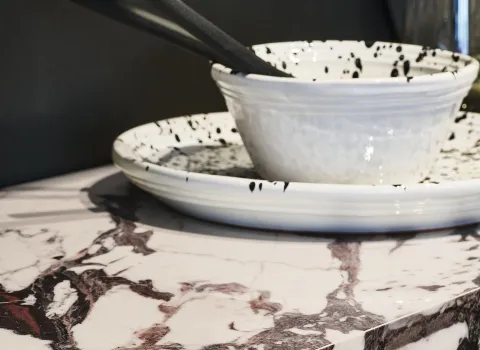 Eine Marmorküchenarbeitsplatte mit markanter braun-weißer Maserung. Darauf stehen zwei schwarz-weiß gesprenkelte Schalen mit schwarzen Stäbchen. Naturstein.