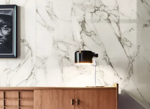 Holz-Sideboard mit Nachttisch-Lampe vor Wand mit Fliesen in Marmoroptik von Marazzi.
