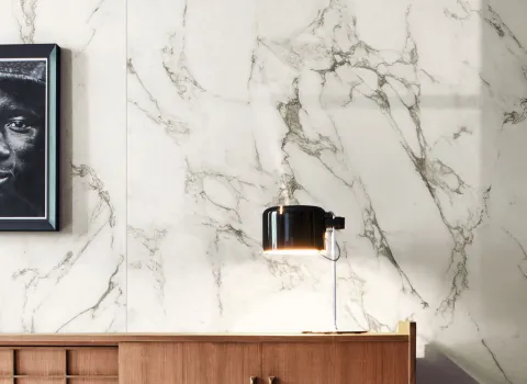 Holz-Sideboard mit Nachttisch-Lampe vor Wand mit Fliesen in Marmoroptik von Marazzi.