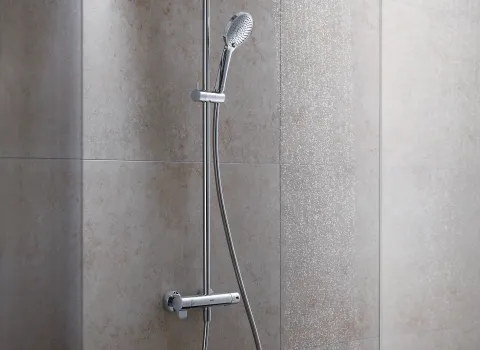 Ein Duschsystem mit glänzender Aufputzarmatur, bestehend aus einem Duschkopf und einem flexiblen Brauseschlauch, installiert an einer beigen Fliesenwand.