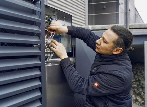 Ein Techniker überprüft eine Elektroinstallation an einer Außeneinheit, während er sorgfältig Kabel in einem offenen Schaltkasten anschließt.