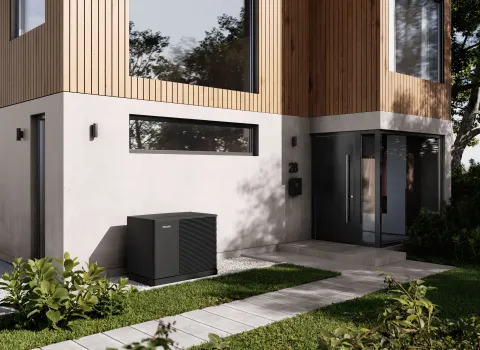 Moderne Wärmepumpe vor einem zweistöckigen Einfamilienhaus mit Holz- und Betonfassade.