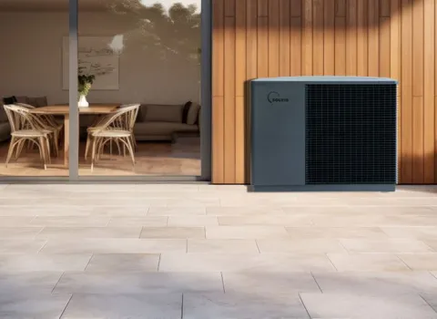 Eine Solvis-Wärmepumpe steht auf einer großzügigen Terrasse vor einer modernen Hausfassade mit Holz- und Glasflächen.