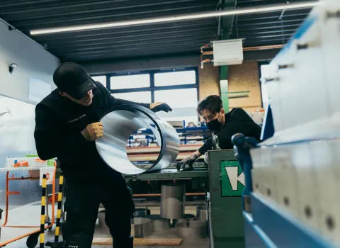 Zwei Flaschner bei der Metallarbeit in einem Arbeitsraum.