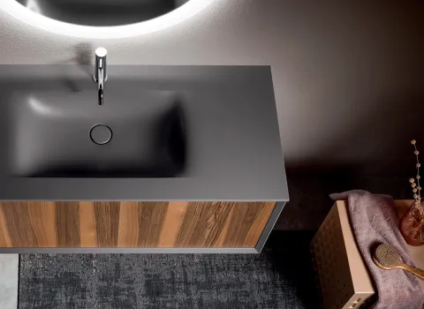 Detailansicht des Waschtischs Stocco Iks Up mit grauer Oberfläche und Front in natürlicher Holzoptik unter rundem Spiegel.