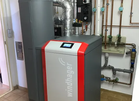 Eine moderne Windhager-Heizungsanlage mit grauem Gehäuse und roten Seitenelementen steht in einem sauber installierten Heizungsraum.