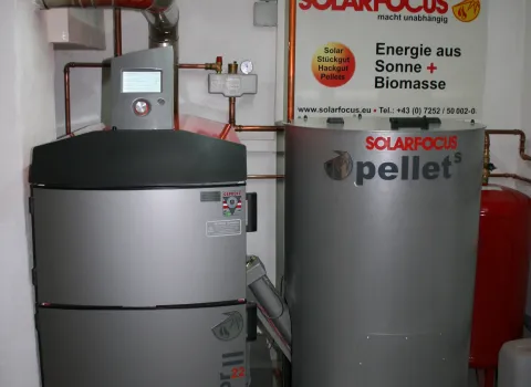 Ein moderner Pelletkessel von SOLARFOCUS steht in einem Technikraum neben einem großen zylindrischen Pelletsspeicher.