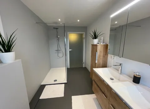 Referenz-Badezimmer mit Walk-In-Dusche, Leuchtspiegel und Badmöbeln aus Holz.