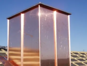 Kupferverkleidung eines Kamins auf einem geneigten Ziegeldach, ausgeführt als langlebige und witterungsbeständige Kaminabdeckung.