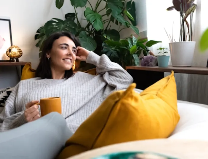 Enntspannte Frau auf Couch mit Teetasse.