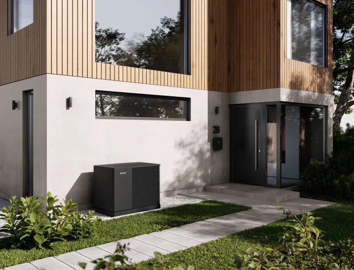 Moderne Wärmepumpe vor einem zweistöckigen Einfamilienhaus mit Holz- und Betonfassade.
