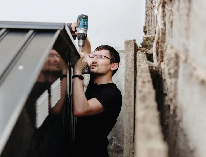 Ein junger Handwerker befestigt Schrauben an einem Metalldach.